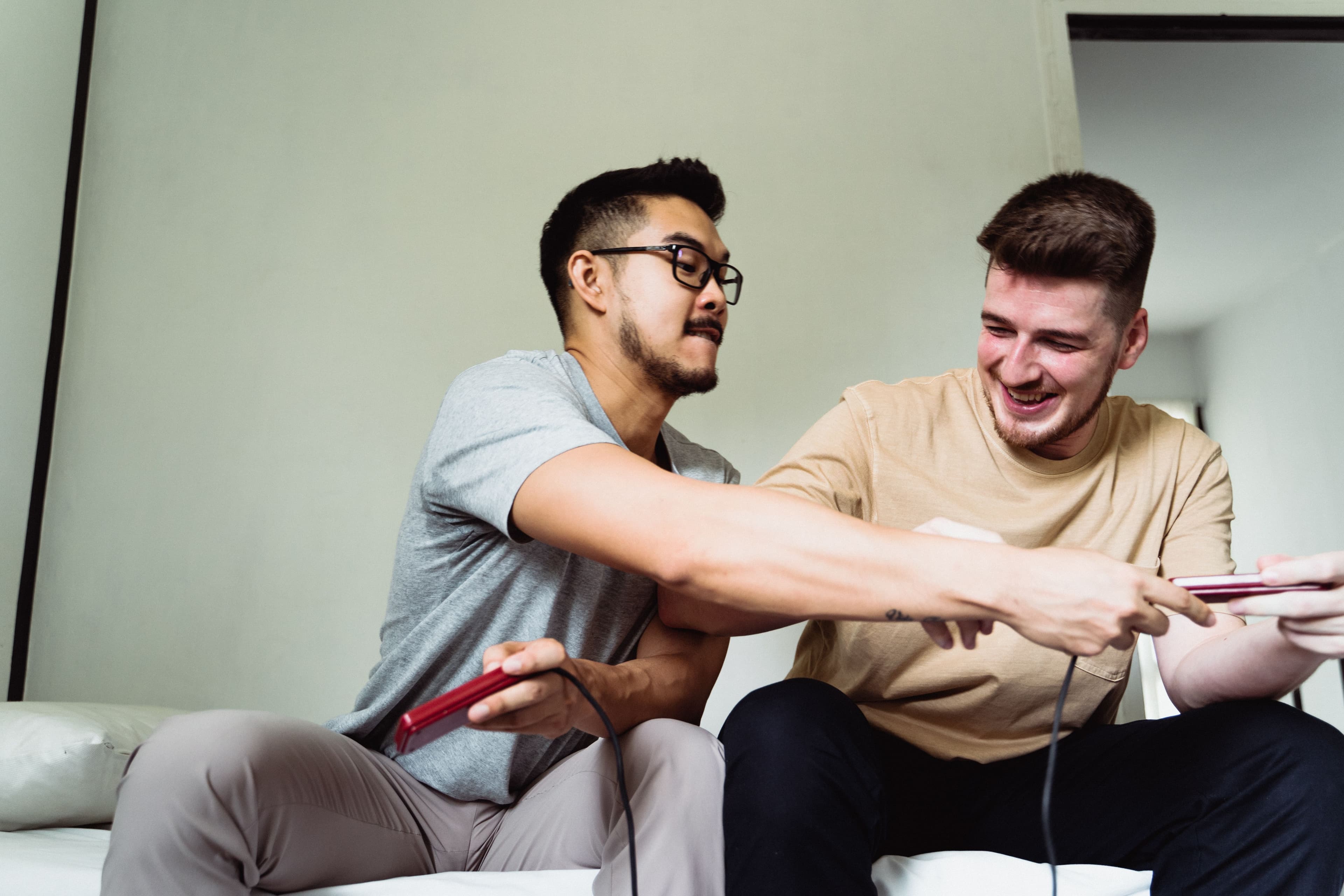 Two friends sitting on a couch, laughing and playing video games in the living room.